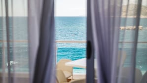 Une vue sur la mer à travers des rideaux, avec une chaise et une table visibles au premier plan.