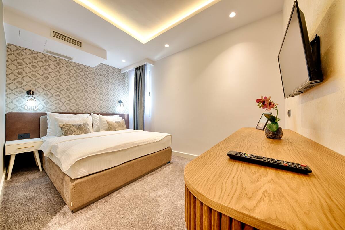 Un dormitorio moderno con cama, mesita de noche, televisor y control remoto sobre una mesa de madera.
