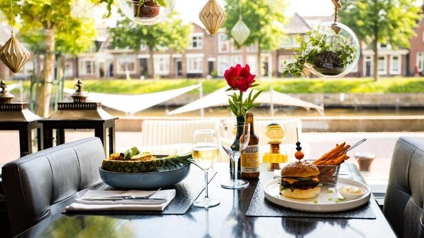 A dining table with a bowl of salad, a burger, and a glass of wine.
