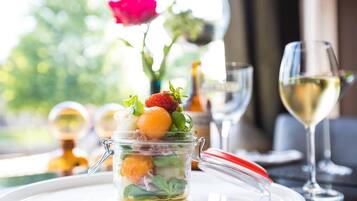 A glass jar with a handle containing a layered salad with strawberries and orange segments, placed on a white plate.