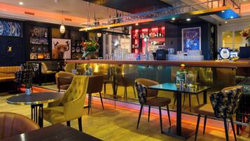 A bar area with a counter, chairs, and tables. There are shelves with bottles and glasses.