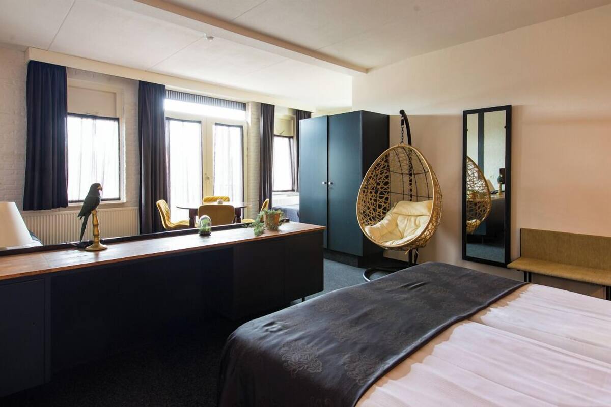 A hotel room with a bed, desk, chair, wardrobe, and a hanging chair.