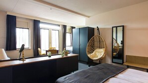 A hotel room with a bed, desk, chair, wardrobe, and a hanging chair.