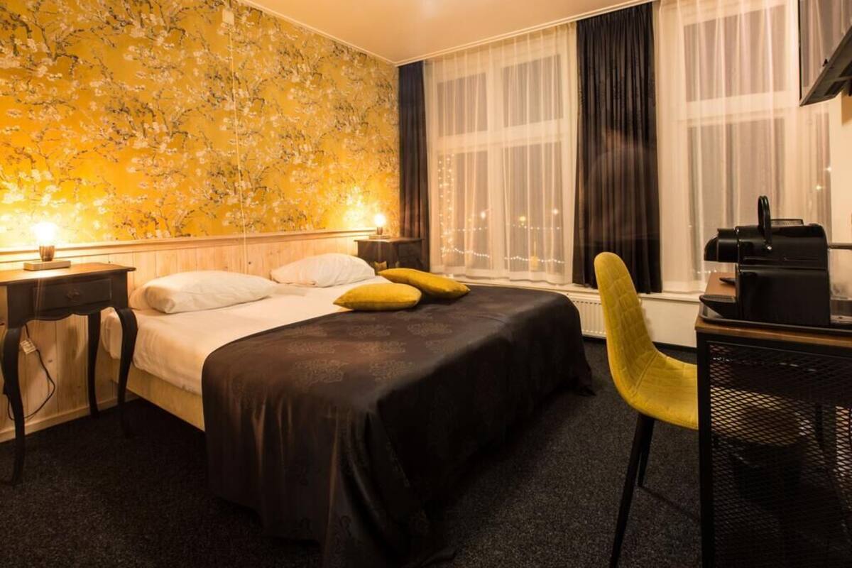 A hotel room with a bed, a desk, a chair, and a window with curtains.