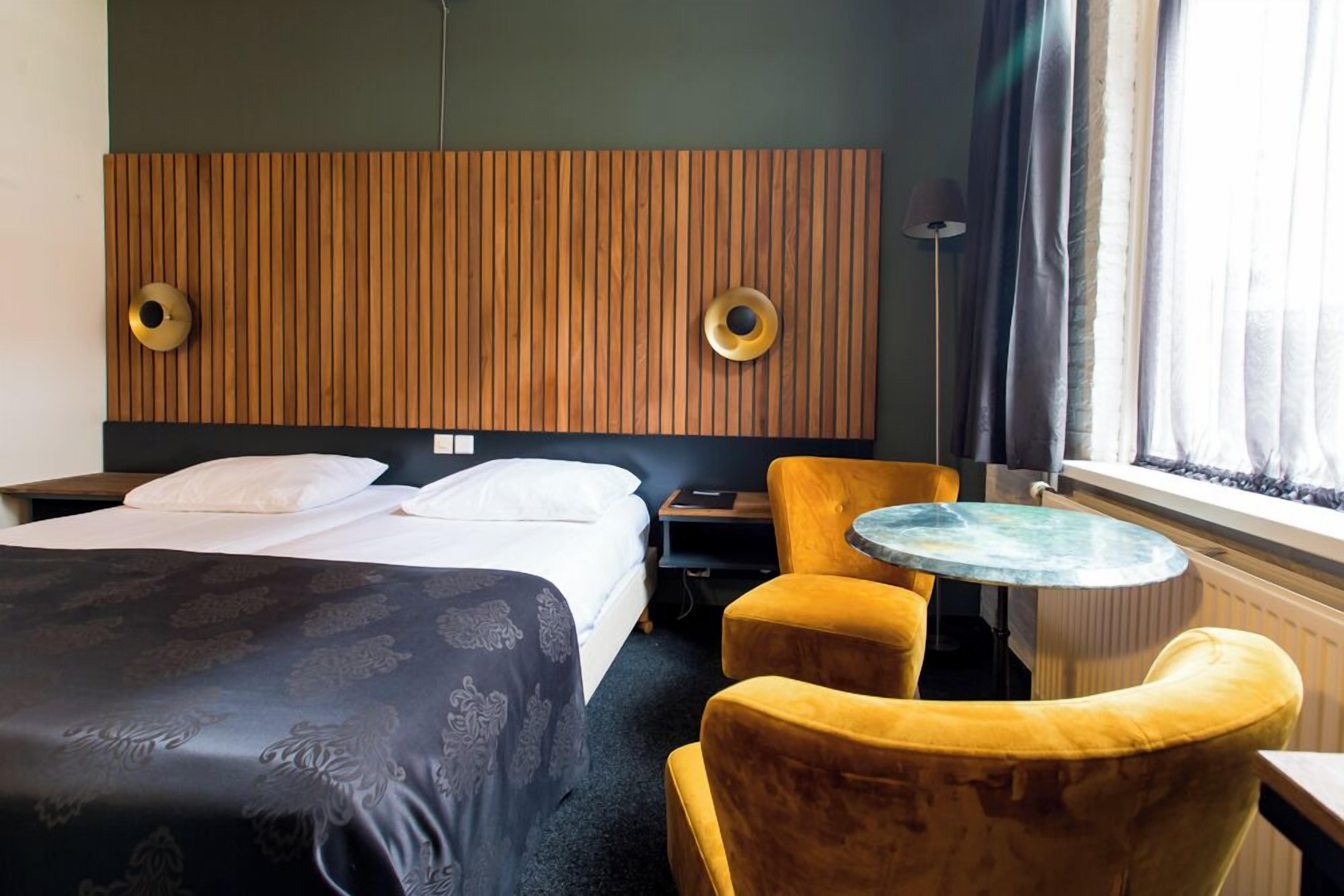 A hotel room with a bed, two chairs, a small table, and a radiator.