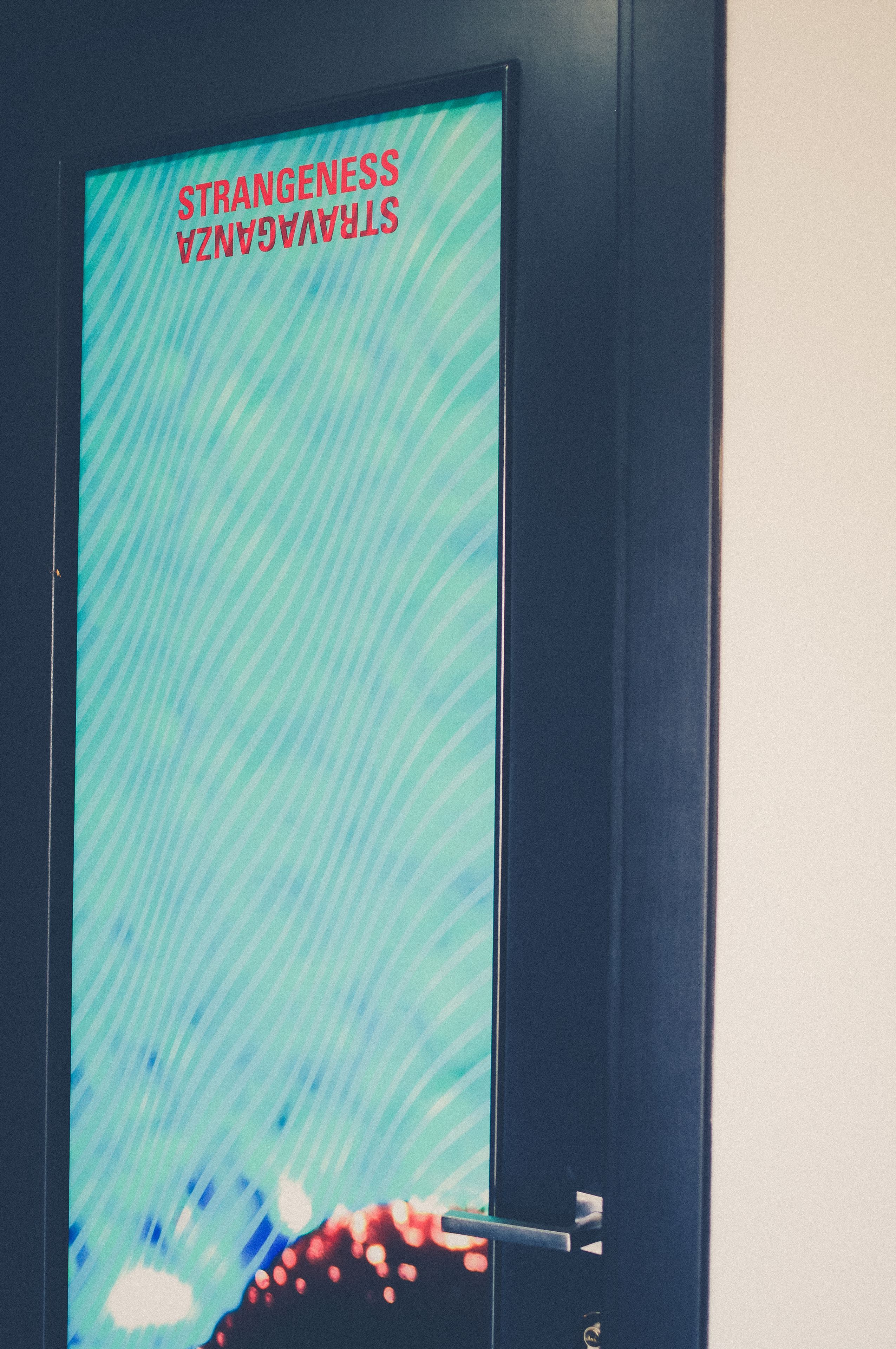 A door with a digital display reading "STRANGENESS STRANGERS" and a keyhole.