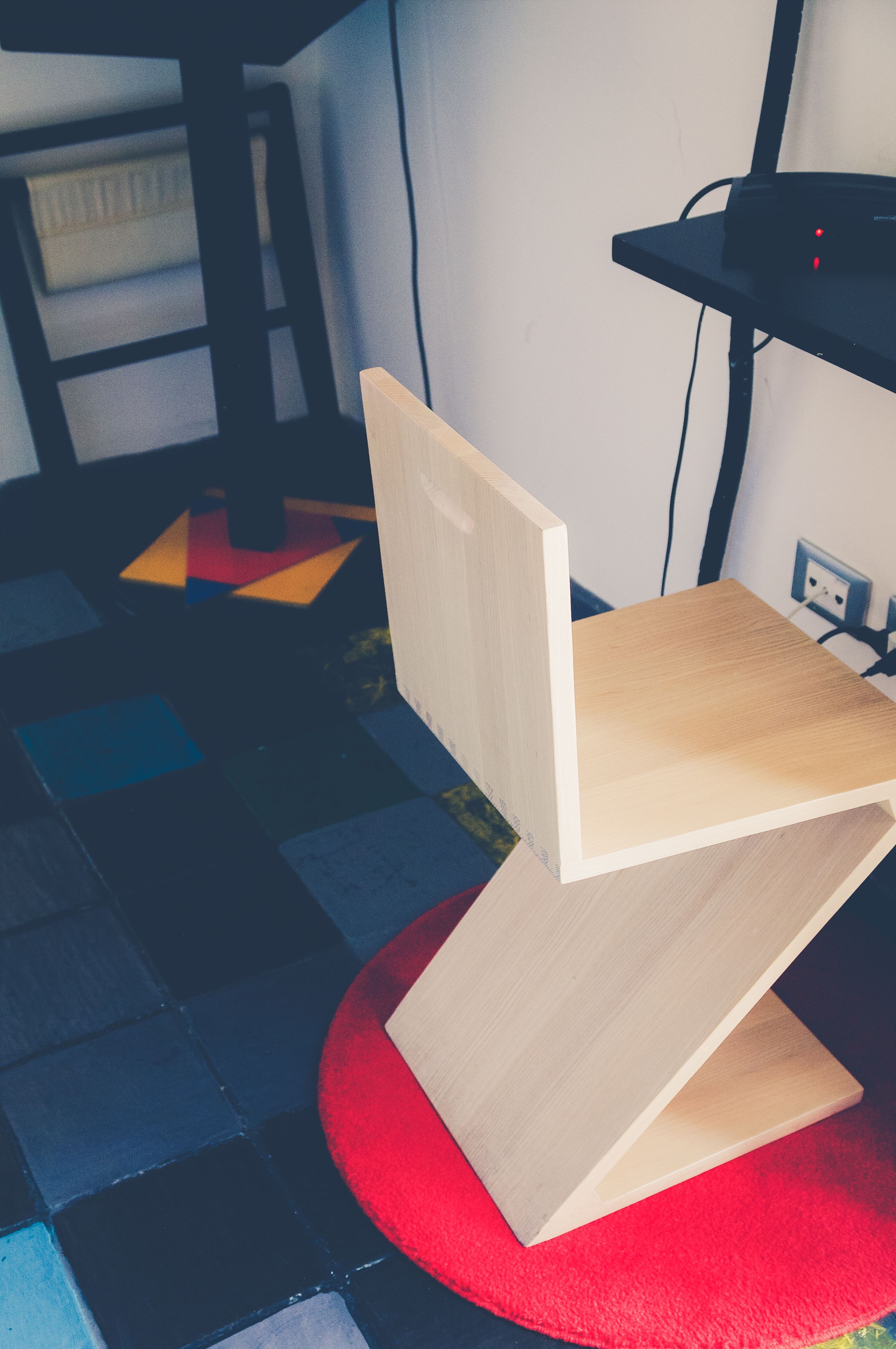 A chair with a wooden backrest and seat, placed on a red circular mat.