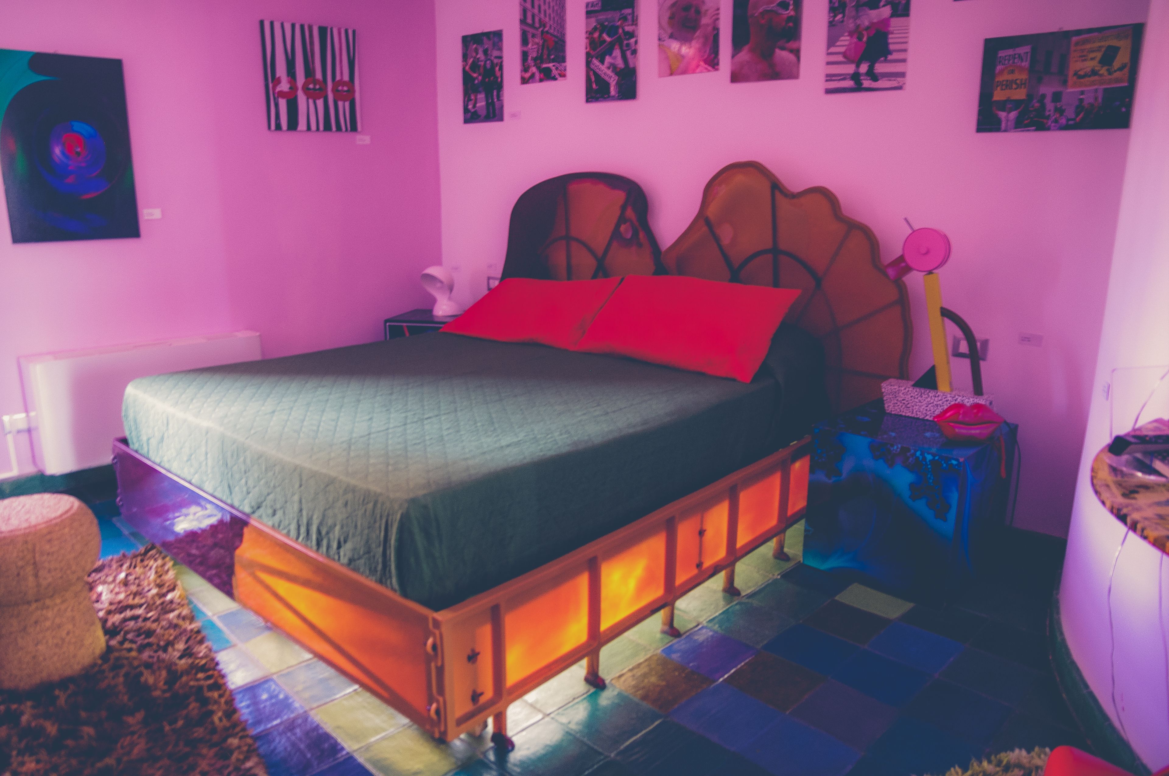 A bedroom with a bed, a nightstand, a lamp, and a wall with pictures.