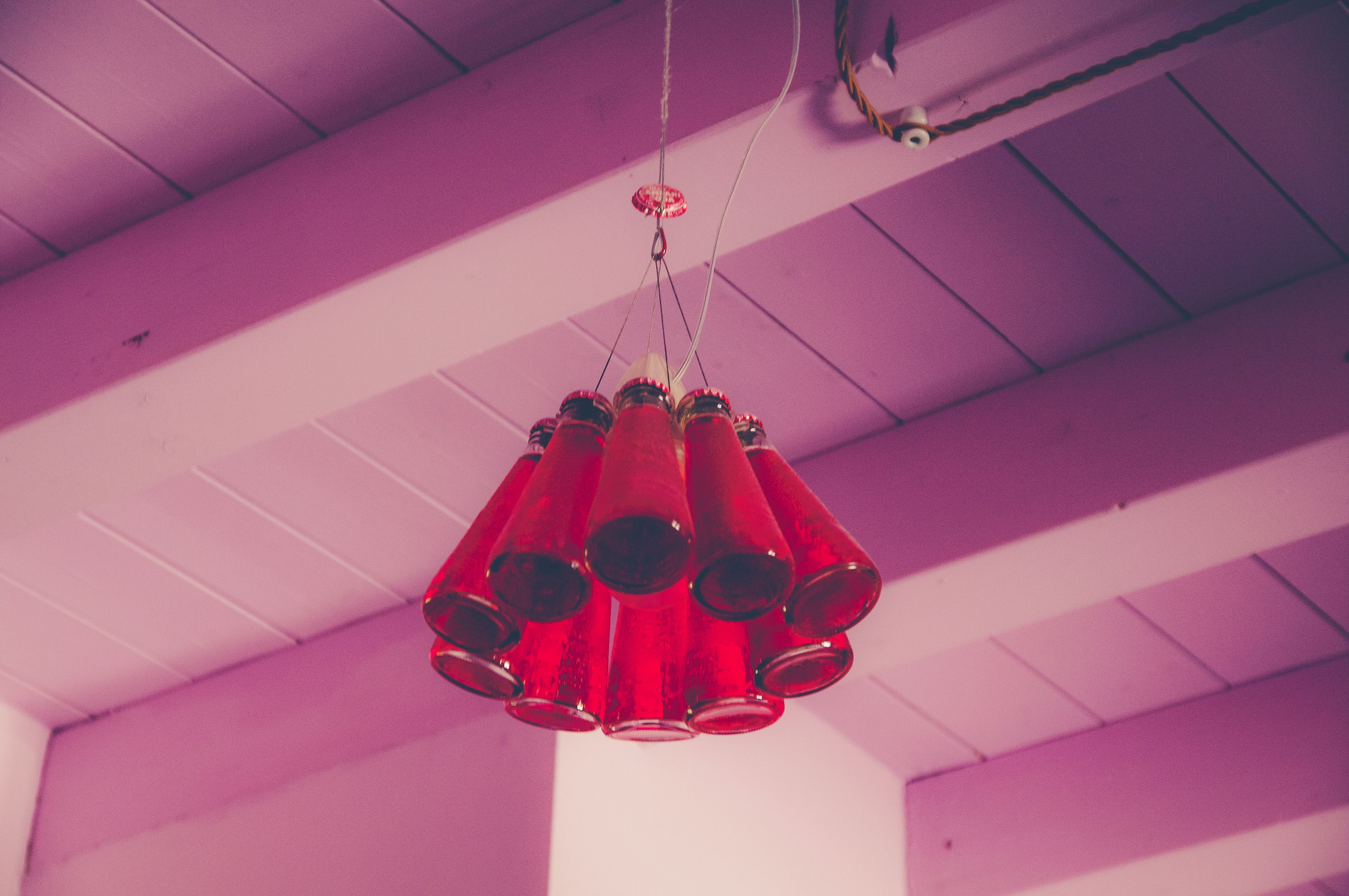 A ceiling with a unique chandelier made of red glass bottles.