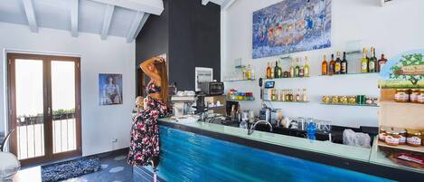 Una zona de bar con mostrador azul, varias botellas y un cuadro en la pared.
