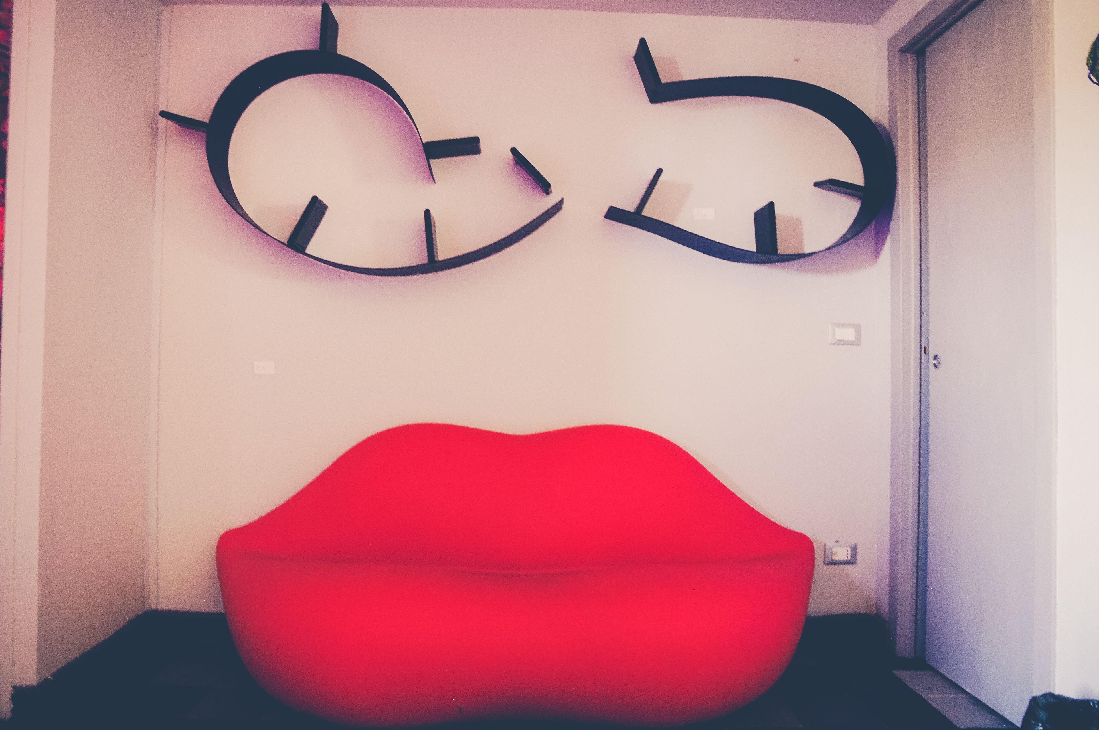 Una habitación con un sillón de peluche rojo y dos relojes de pared.