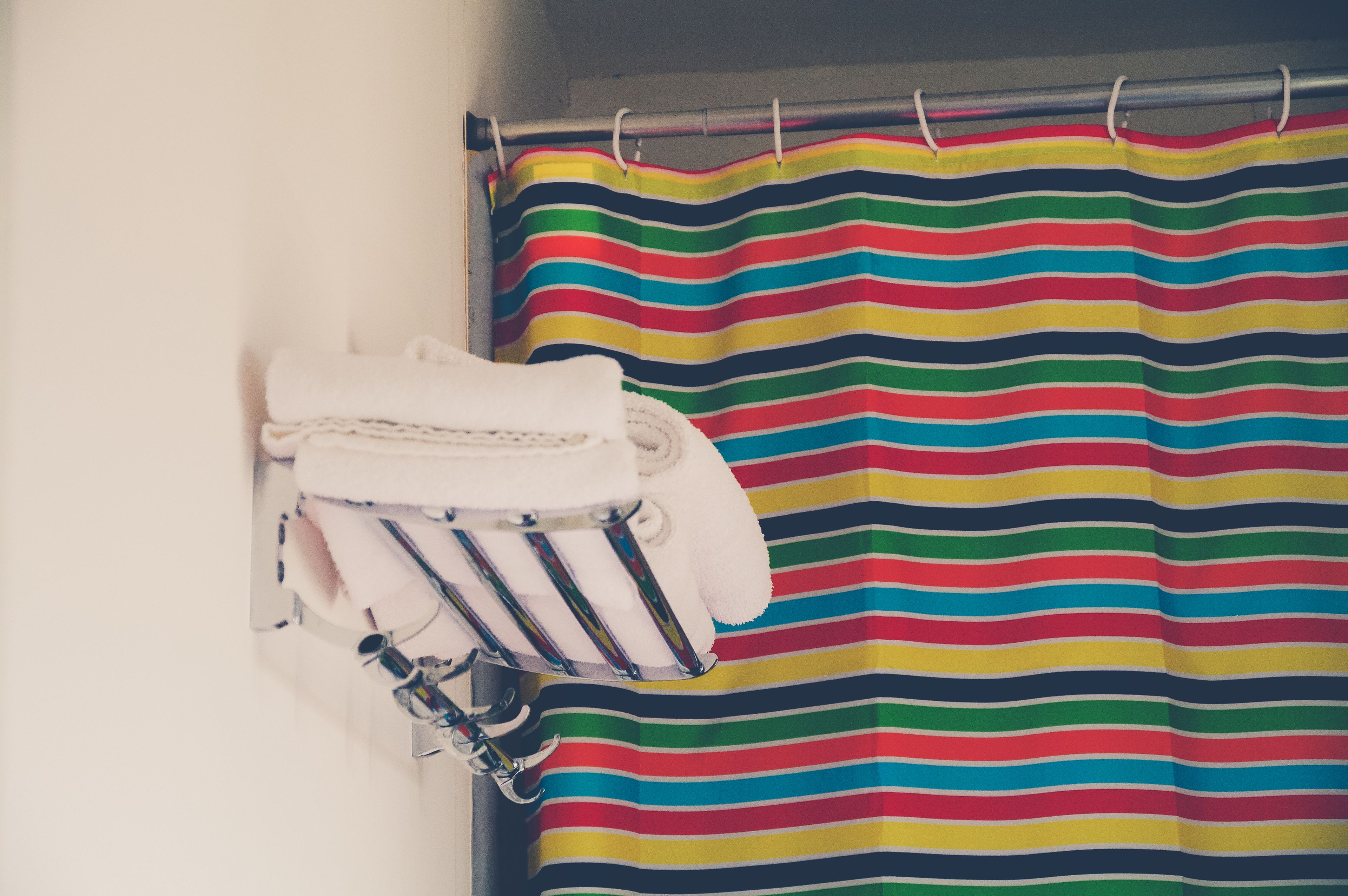 Un bagno con tenda da doccia a righe, un porta asciugamani con un asciugamano piegato e un altro porta asciugamani a parete con un asciugamano.