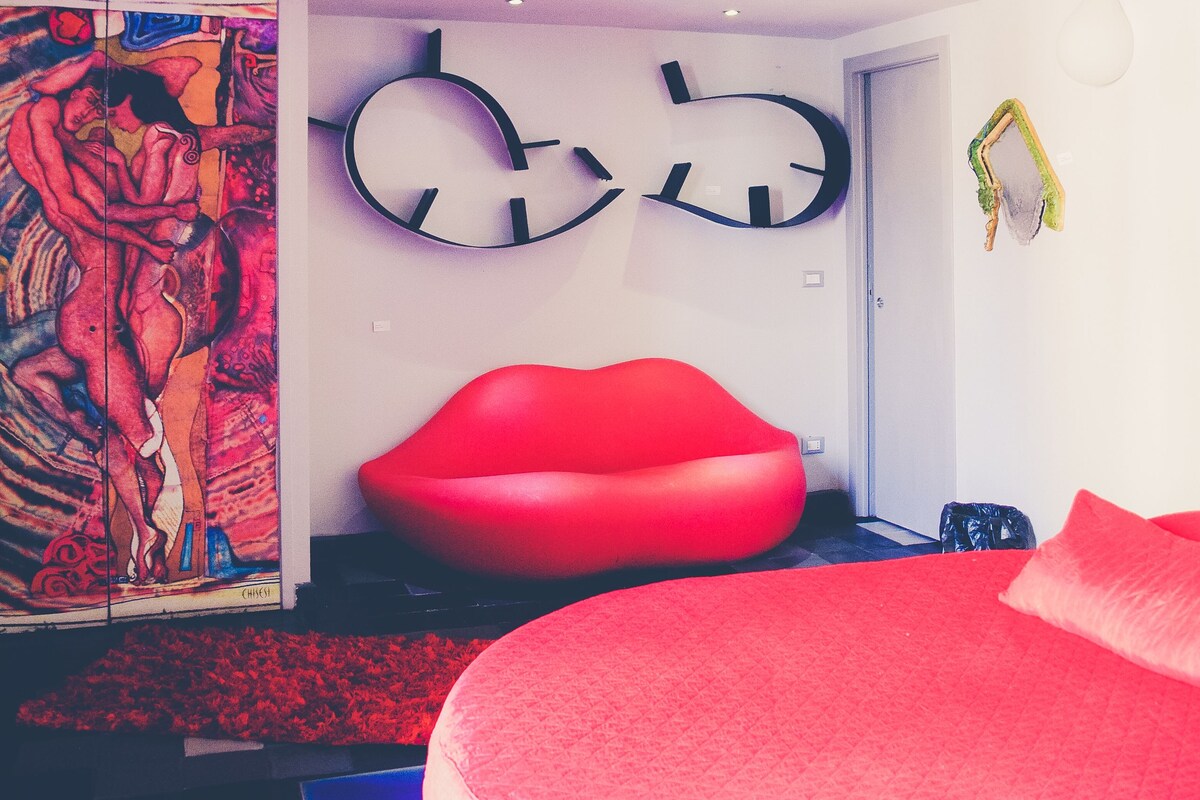 A bedroom with a large bed, a red bean bag chair, a wall clock, and a mural.