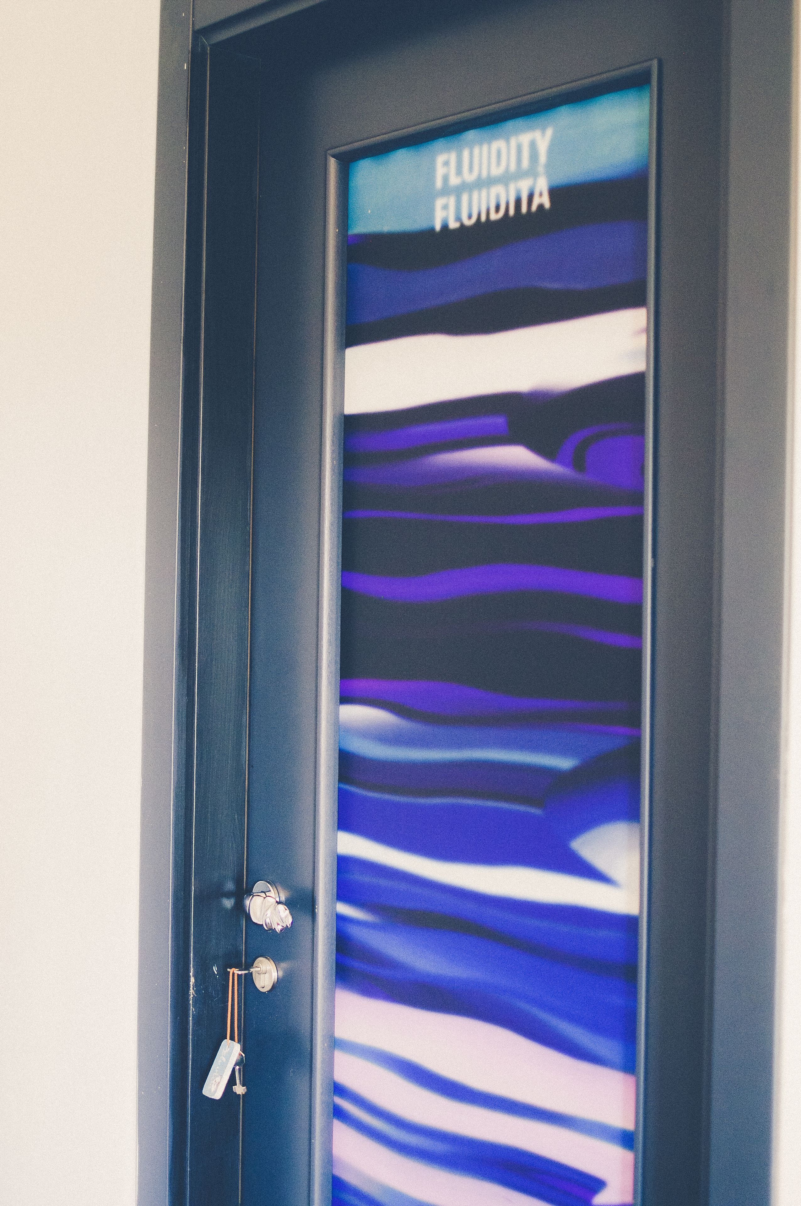 A door with a glass panel displaying a blue and purple abstract design and the text "FLUIDITY FLUIDITA".