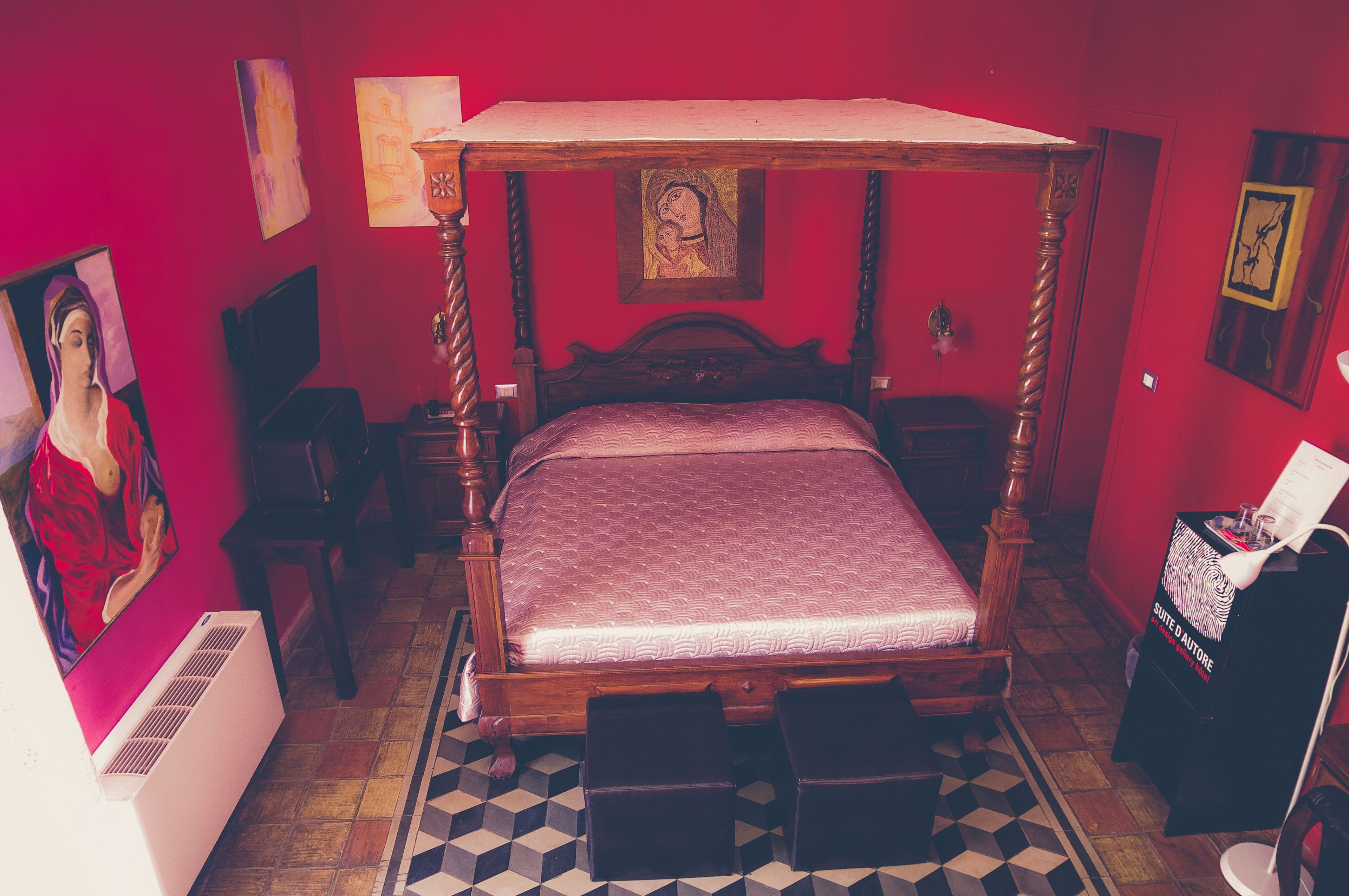 A room with a four-poster bed, a radiator, a chair, and a small table with a lamp.