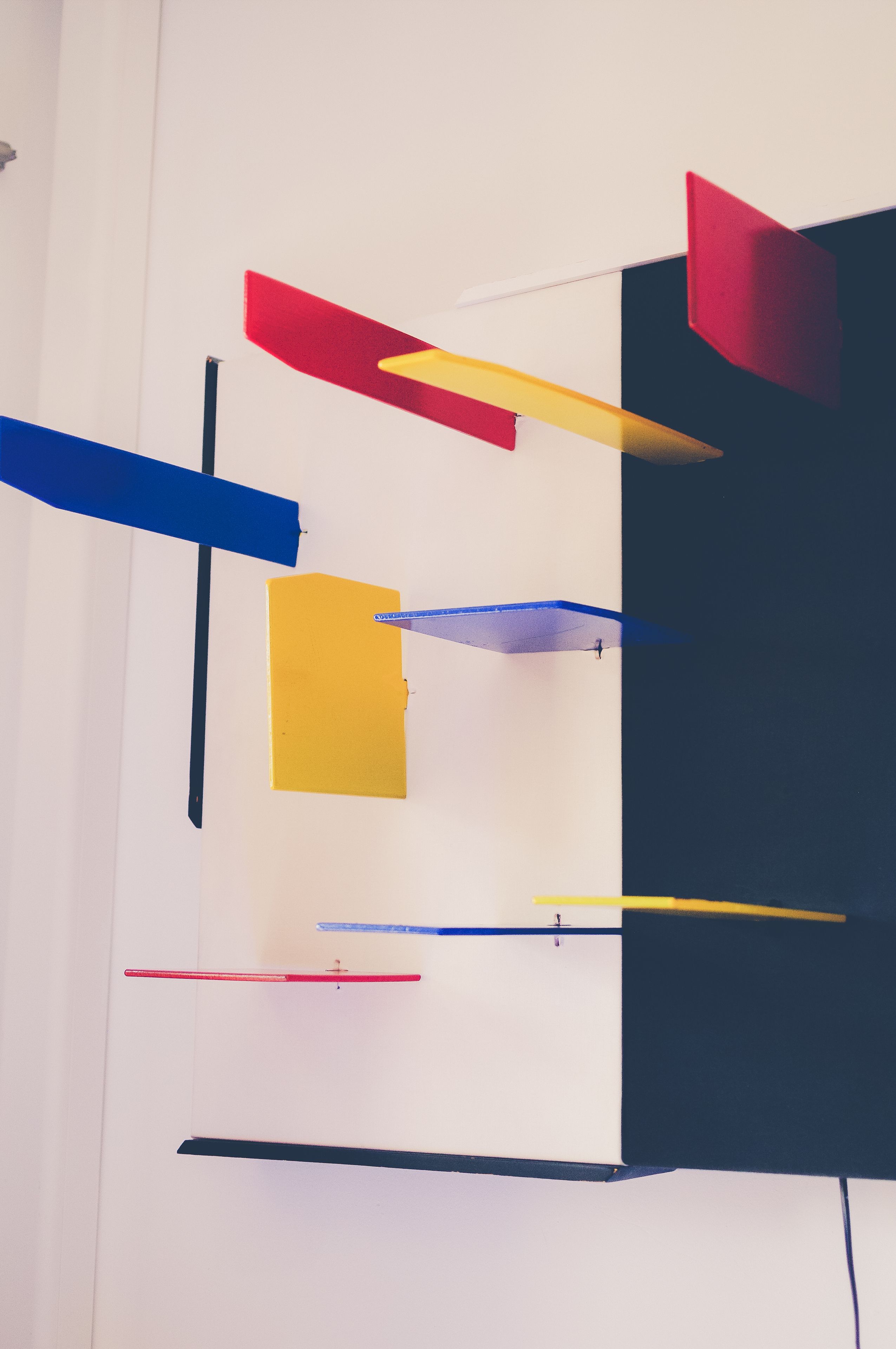 A room with a white wall and a black partition. There are several colorful objects hanging from the ceiling, including red, yellow, and blue items.