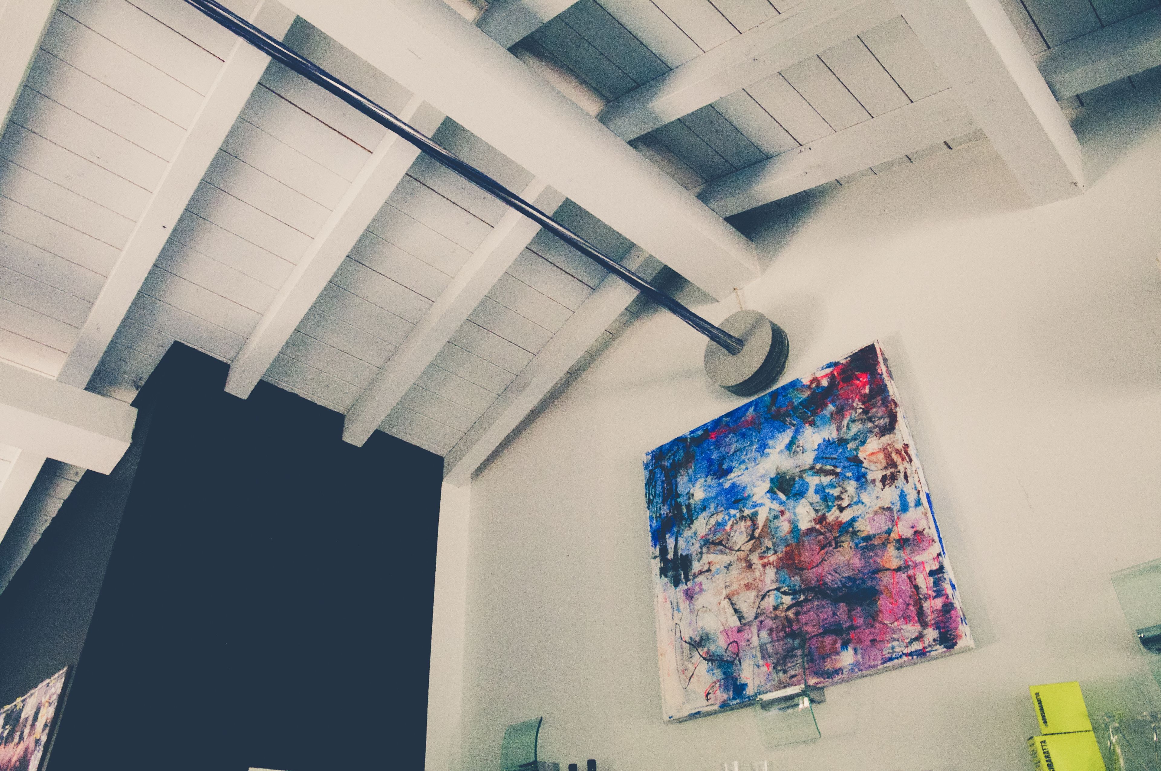 A room with a high ceiling, exposed beams, and a large abstract painting on the wall.