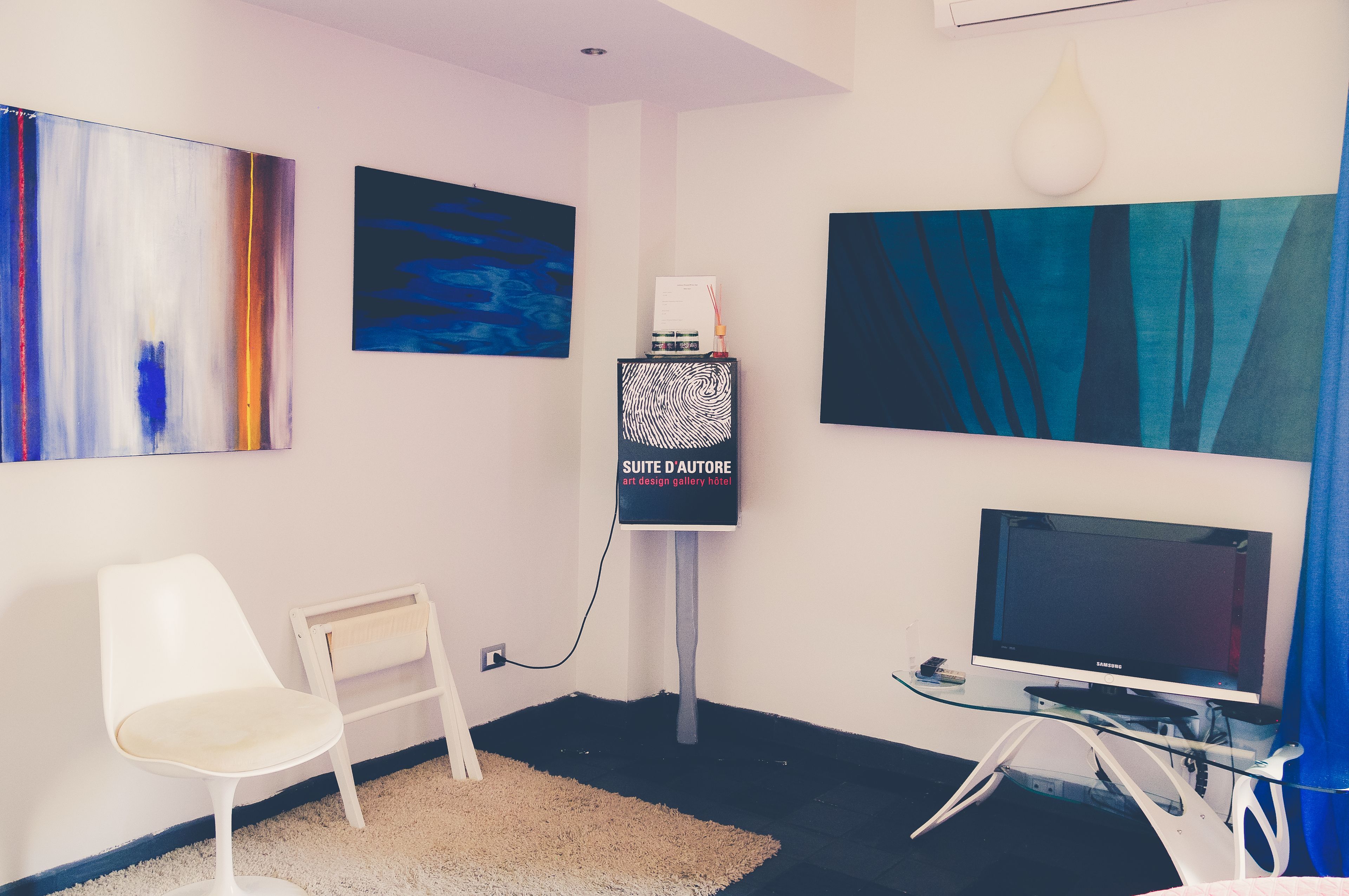Ein modernes Hotelzimmer mit Flachbildfernseher, einem weißen Sessel und abstrakter Kunst an den Wänden.