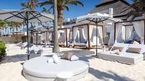 Un complexe hôtelier en bord de mer, doté de chaises longues, de parasols et d’un bâtiment à toit de chaume.