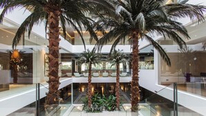 Un atrium à plusieurs niveaux, agrémenté de palmiers, de rampes en verre et d’un espace de repos central.