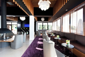 Een moderne lobby met een paars tapijt, zithoeken en grote ramen.