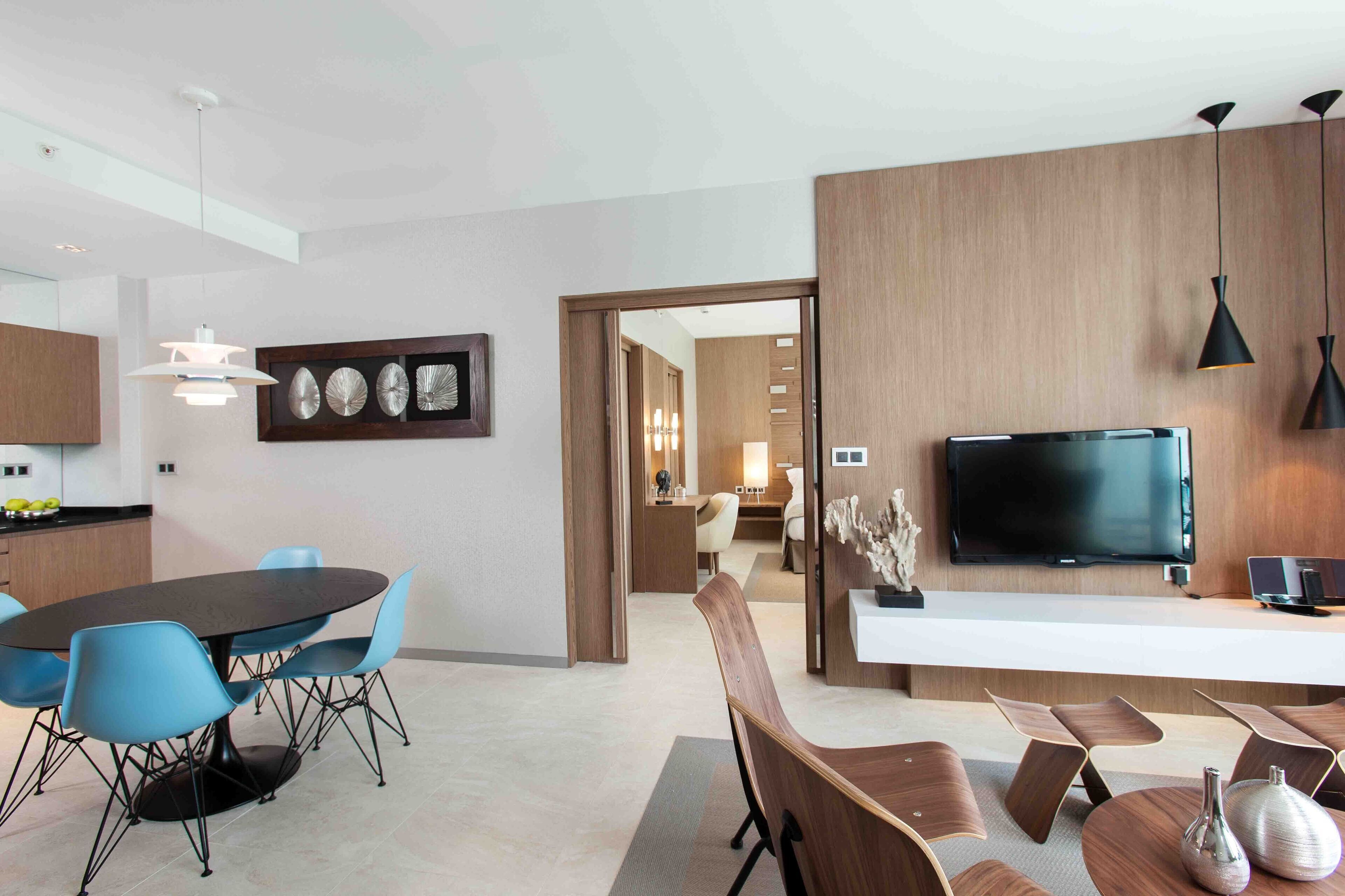 A modern kitchen with a dining area, a TV, and a wooden accent wall.