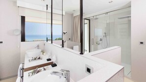 Une salle de bain moderne dotée d’une grande fenêtre, d’une douche en verre et d’un meuble-lavabo avec un évier et un miroir.