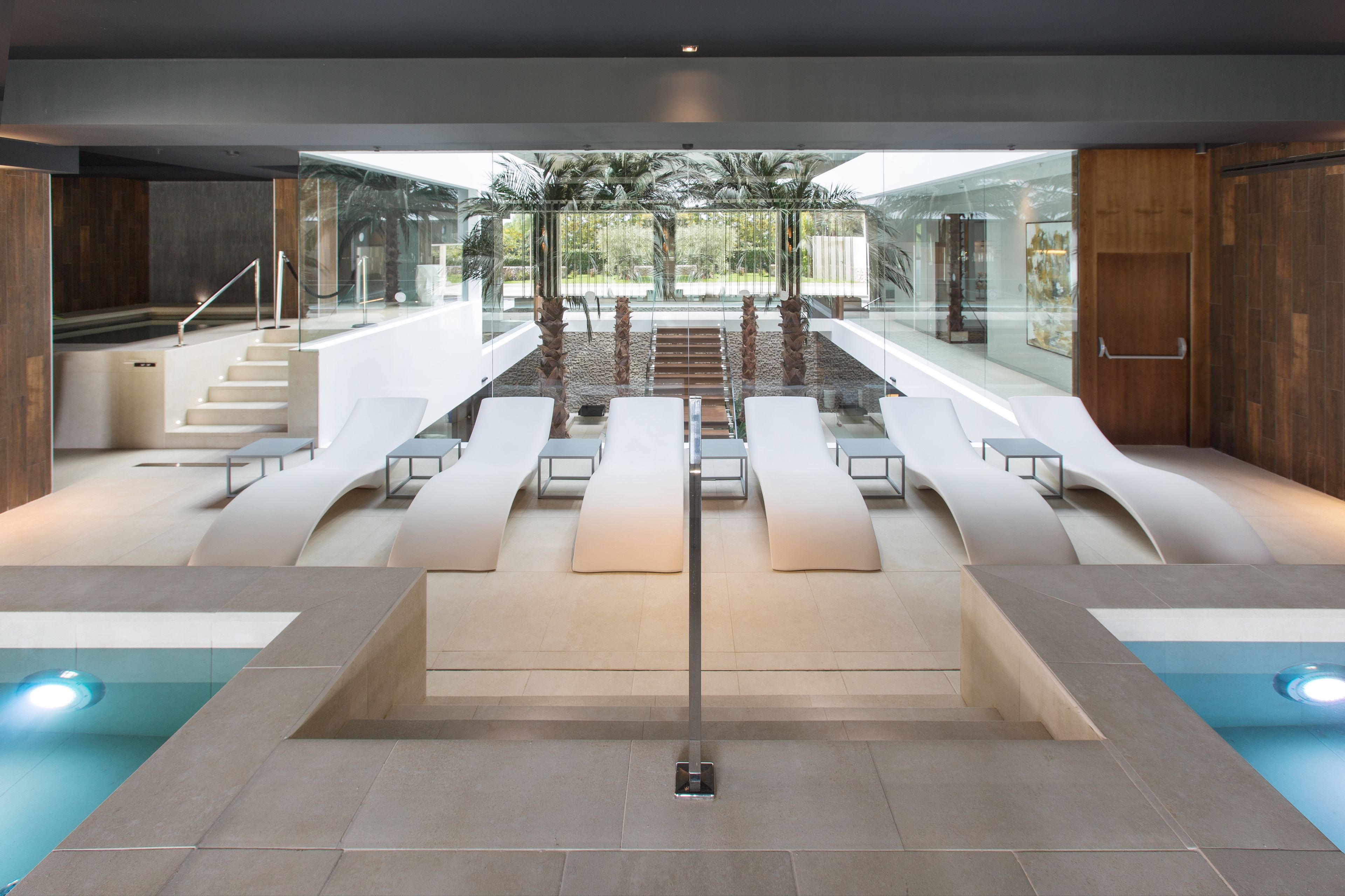 A modern indoor pool area with a glass ceiling, seating along the sides, and a central staircase.