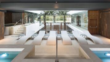 A modern indoor pool area with a glass ceiling, seating along the sides, and a central staircase.