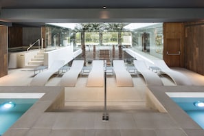A modern indoor pool area with a glass ceiling, seating along the sides, and a central staircase. - The Oasis by Don Carlos Resort (Marbella)