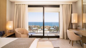 Une chambre d’hôtel équipée d’un lit, d’un bureau, d’une chaise, d’une télévision et offrant une vue sur l’océan grâce à une porte coulissante.