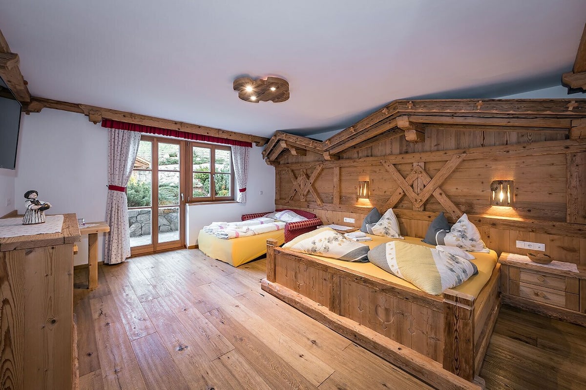 Ein rustikales Zimmer mit Holzboden, einem Bett, einem kleinen Tisch und einem Fenster mit Vorhängen.
