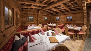 Una cabaña rústica de madera con varias mesas y bancos, cada conjunto con manteles blancos y servilletas a cuadros rojos.