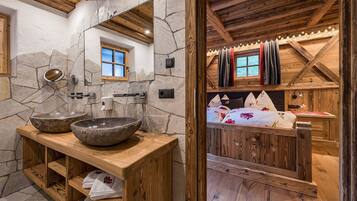 Un baño rústico con lavamanos de piedra, tocador de madera y pared espejada.