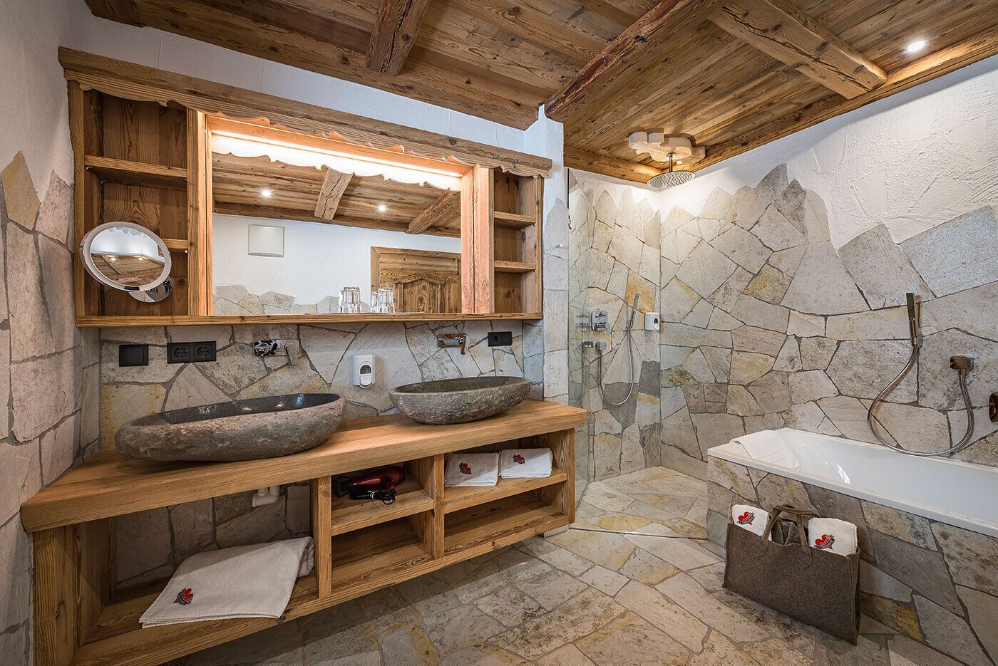 Un baño rústico con paredes de piedra, repisas de madera y un espejo grande.