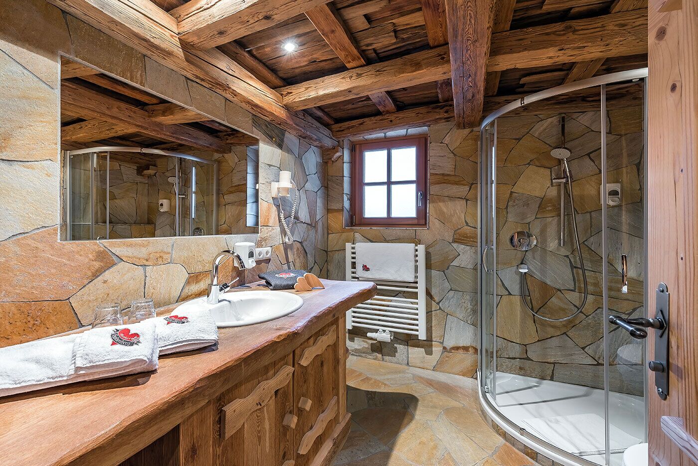 Een badkamer met een stenen muur, een houten wastafelmeubel en een douchecabine met glazen wanden.