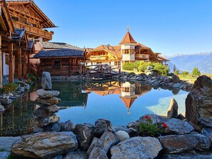 A traditional wooden chalet with a reflection pool and a stone bridge. - Almdorf Haidenberg (San Lorenzo di Sebato)