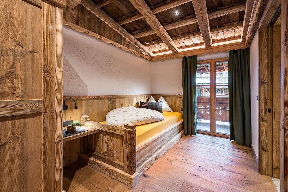Ein Schlafzimmer mit Holzboden, einem Bett, einem Nachttisch und einem Fenster mit Vorhängen.