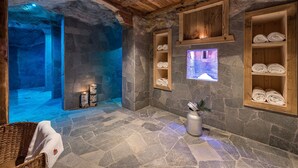 Habitación con paredes de piedra, estantes de madera con toallas, suelo de piedra y techo de madera.