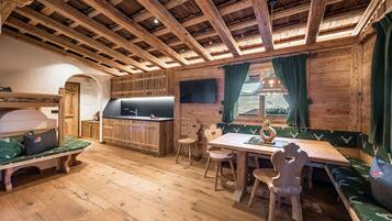 A rustic cabin interior with wooden beams, a kitchenette, a dining area with benches, and a cozy seating area.