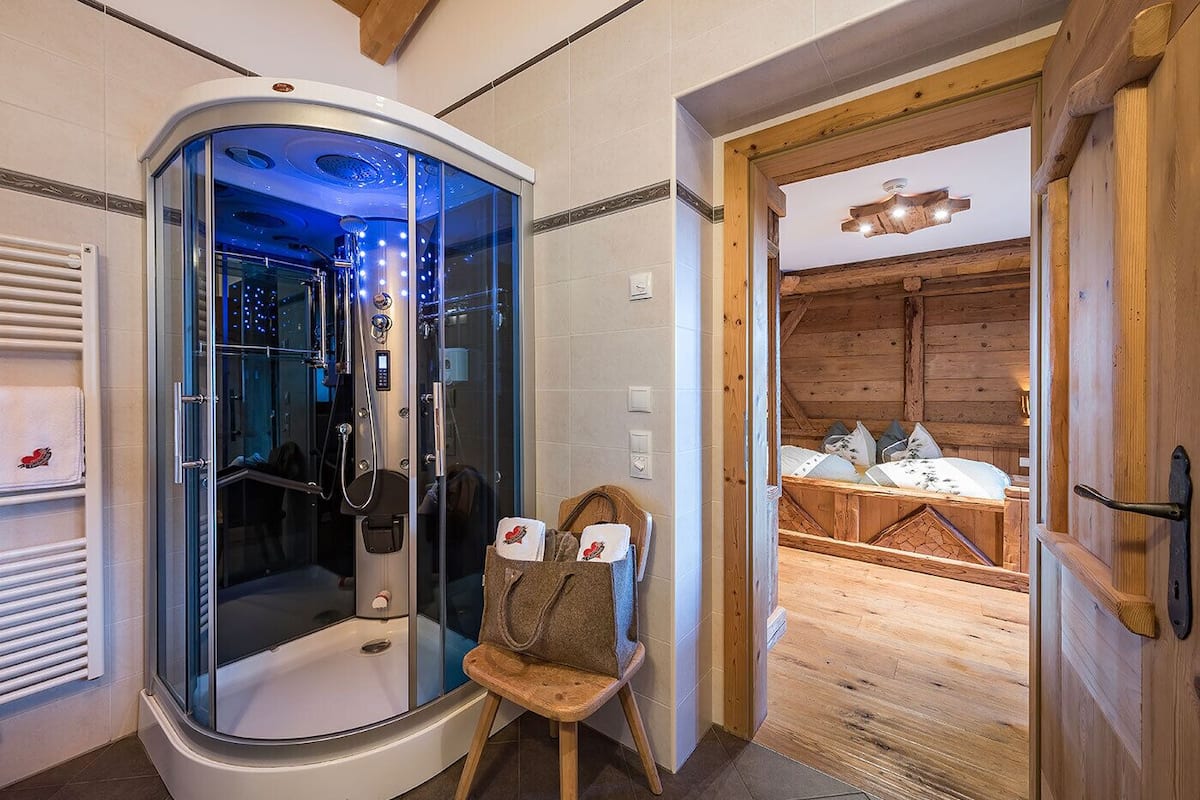 Ein modernes Badezimmer mit einer einteiligen Glasdusche, Holzboden und einem hölzernen Bett im angrenzenden Zimmer.