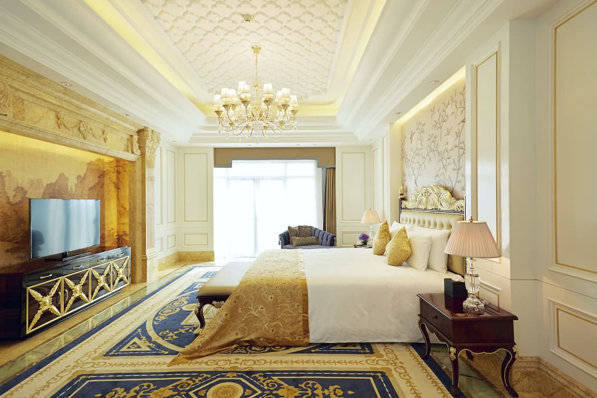 A luxurious hotel room with a large bed, a chandelier, a television, and a decorative wall.