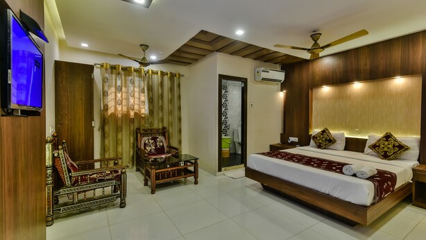 A well-lit bedroom with a large bed, a wooden headboard, a ceiling fan, and a television on the wall. - Hotel Guest Inn Residency (Mumbai)