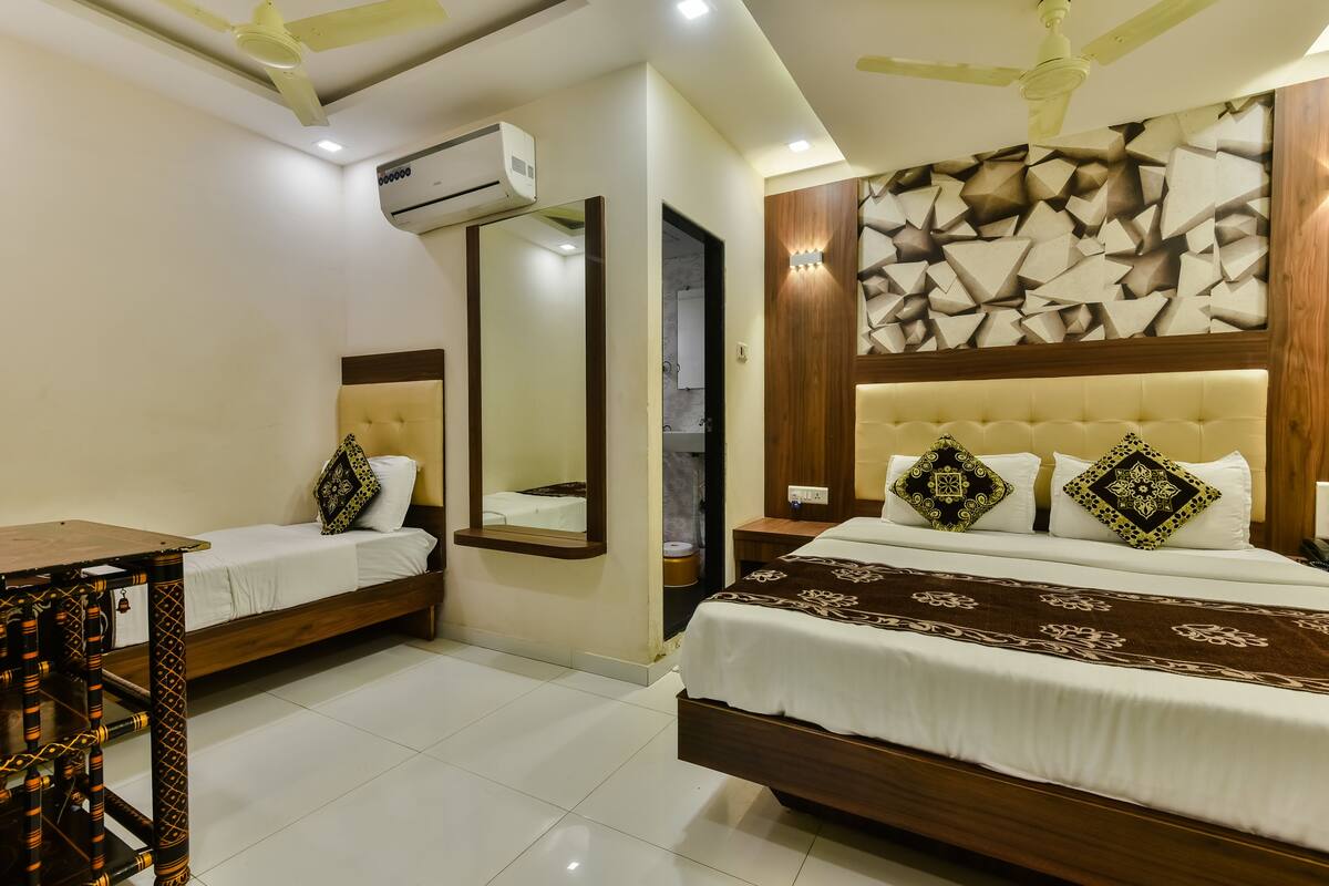 A hotel room with two beds, a mirror, a ceiling fan, and a wall-mounted air conditioner.