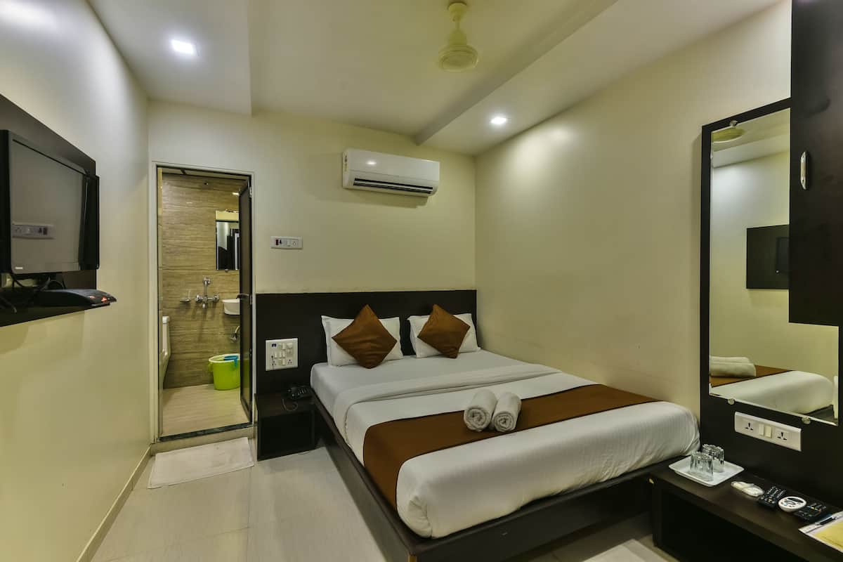 A hotel room with a bed, bedside table, mirror, air conditioning unit, and a view of the bathroom.