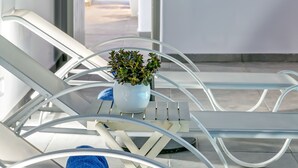 Ein Balkon mit weißen Metallstühlen, einem kleinen Topfpflanzen und Blick auf einen Raum mit Bett und Vorhängen.