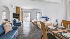 Ein modernes Hotelzimmer mit einer Couch, zwei Betten, einem Esstisch und einem Fernseher.