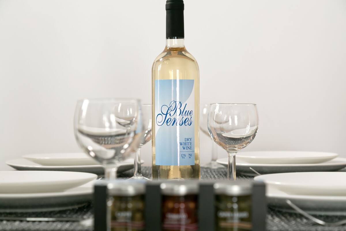 A bottle of Blue Tenses dry white wine on a table with two empty wine glasses.