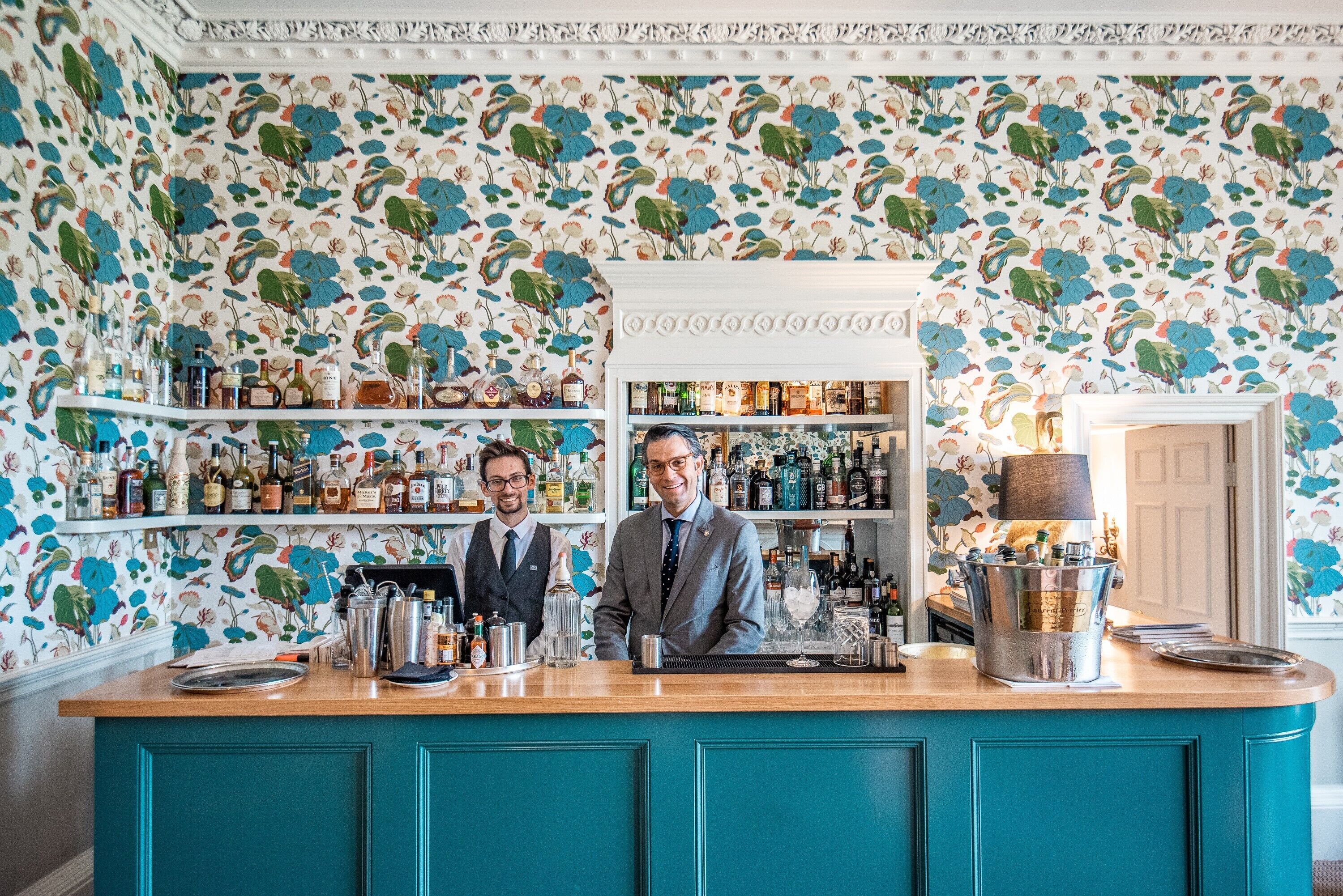 Eine Bar mit türkisfarbenen Schränken und einem floralen Wandhintergrund.