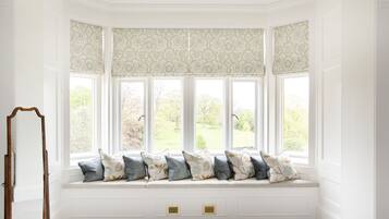 A bay window with patterned curtains, a bench with cushions, and a mirror.